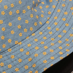 Detailed close-up of light blue denim bucket hat with yellow floral print and stitching