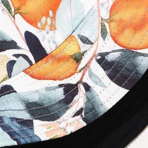 Macro detail of bucket hat showing vibrant orange fruit print and precise parallel stitching