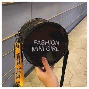 Detail of round black patent leather crossbody bag with bold yellow strap decoration