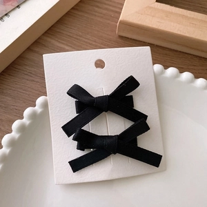 Close-up of two elegant black ribbon bow hair clips on a minimalist display card