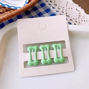 Three mint green bone-shaped hair clips displayed on a cream accessories card
