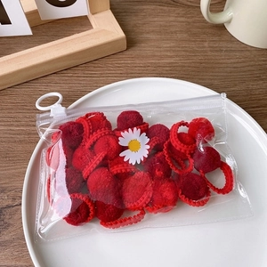 Macro detail of red fuzzy pom-pom hair ties in a daisy print transparent zipper bag