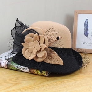 Detail of wool cloche hat with floral mesh veil and feathers on a wooden surface