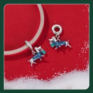 Macro view of silver dachshund charm wearing blue enamel sweater on a snowy red surface