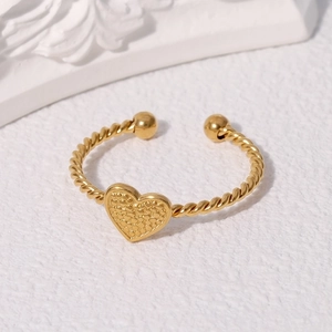 Golden heart ring with textured relief on twisted band shown on elegant white stone