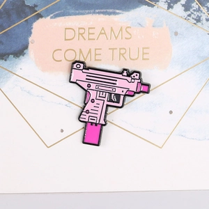Close-up of a pink enamel Uzi submachine gun brooch on a decorative greeting card