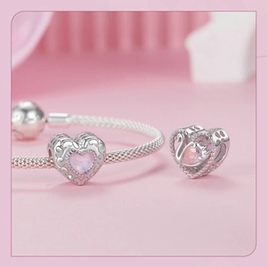 Macro view of a silver heart charm with pink gemstone and swan design on snake chain