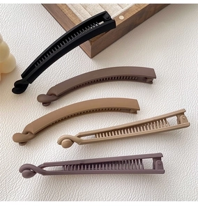 Detail of five matte banana hair clips in neutral colors on a textured surface