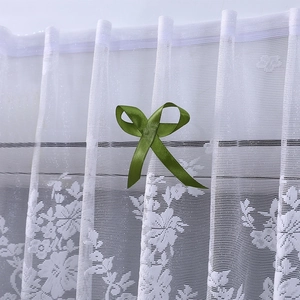 Detalle de cortina de encaje floral blanco con un lazo decorativo de cinta de satén verde