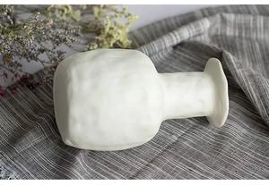 Detailed view of white ceramic vase with rough texture on a striped linen fabric