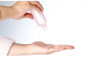 Close-up of a pink glass perfume spray bottle being used by a hand on white background