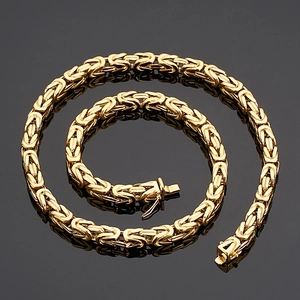 Polished gold stainless steel Byzantine chain necklace coiled on a reflective dark surface