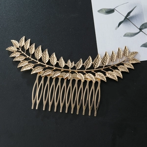 Golden metal leaf hair comb with symmetric foliage pattern on black textured surface