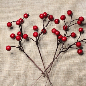 Close-up of three artificial red berry branches on a textured beige burlap background