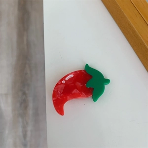 Close-up of a red chili-shaped hair clip made of resin with a green stem leaf