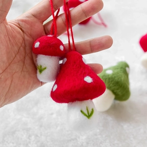 Handmade wool felt mushroom Christmas ornaments in red and green hanging on white fur background