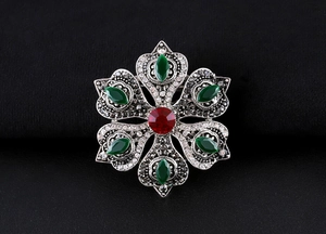 Detailed view of vintage baroque brooch with red and green gems on dark surface
