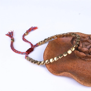 Detalle de pulsera tejida a mano con cuentas de latón y cordón con borla ajustable