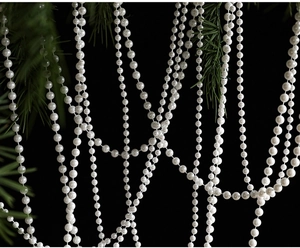 Detail of white pearl bead chain garland draped on green pine branches for Xmas decor