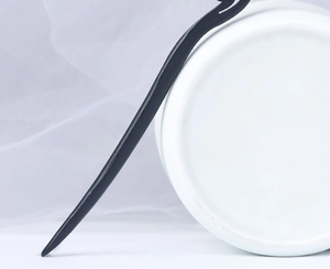 Detail of dark wood hair stick leaning on white ceramic with minimalist curved design