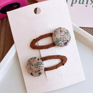 Detalle de pinzas para el cabello con botones florales y tela beige en cartón