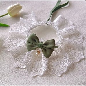 Detailed close-up of white lace pet collar with green satin bow and pearl pendant