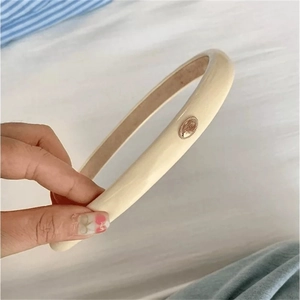 Detail of beige faux leather headband featuring a polished oval gold metal accent