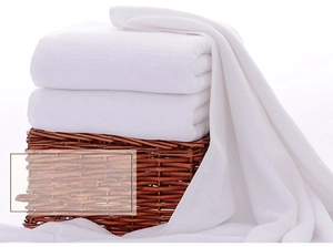 Detail of soft white cotton bath towels folded neatly on a rustic wicker basket