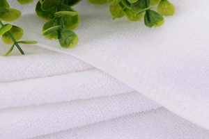 Close-up of white hotel cotton towel showing soft loop texture and natural greenery