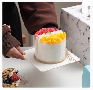 Close-up of white mousse cake with fruit toppings held by hands in front of a white box