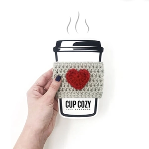 Handmade beige crochet mug sleeve with a red heart detail shown on a white background