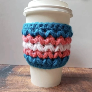 Handmade crochet coffee mug sleeve with blue, pink and white stripes on wooden desk