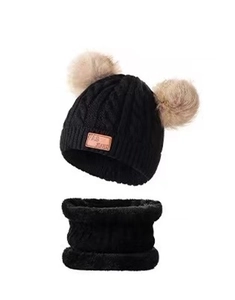 Detailed view of black cable knit hat with dual fur pom-poms and matching fleece scarf