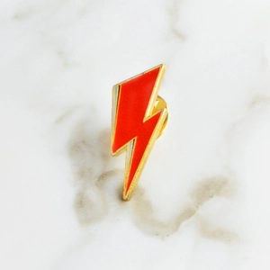 Creative red lightning enamel brooch with golden metal edges on a marble background