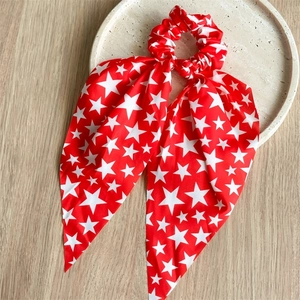 Detail of red hair scrunchie with white stars and bow ribbon on a stone tray