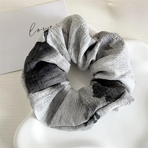 Détail d'un chouchou géant à motif d'encre grise sur un plateau en céramique blanche épuré