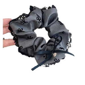 Elegant grey lace scrunchie with black bow pattern and a metallic charm accessory