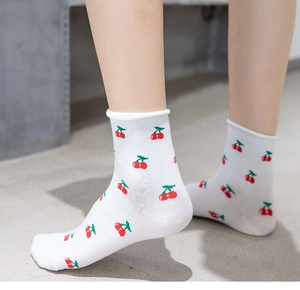 Detail of white cotton sock with cherry pattern and ruffled edge worn by a model
