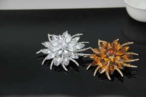 Detail view of two crystal flower brooches in silver and gold plating on a black surface
