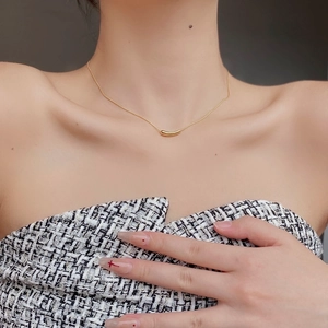 Close-up of a curved golden bean pendant necklace on a delicate chain worn by a model