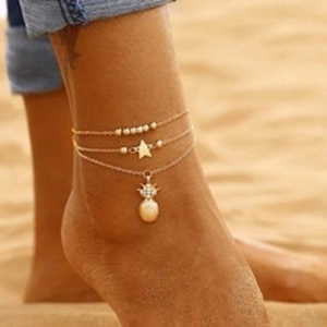 Three-layer gold anklet with pineapple and star charms worn on beach ankle