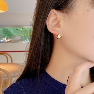 Close-up of elegant gold teddy bear stud earrings worn by a model in a natural setting