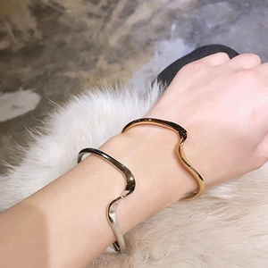 Close-up of gold and silver wavy textured bangles worn on a white faux fur background
