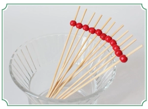 Close-up of bamboo cocktail picks with red beads in a clear glass on white background