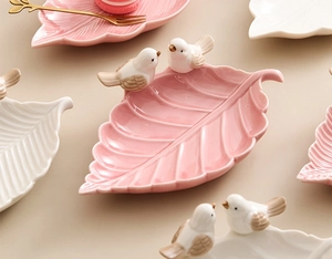 Close-up of pink and white leaf-shaped ceramic jewelry trays with cute bird details