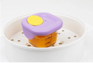 Detail of 200ml glass baby food container with purple lid and volume scale in a steamer