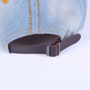 Macro detail of adjustable leather strap and metal buckle on washed denim baseball cap