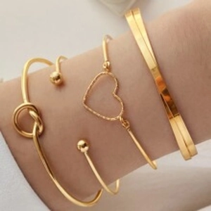 Close-up of four-piece gold bracelet set with knot and heart designs on a model wrist