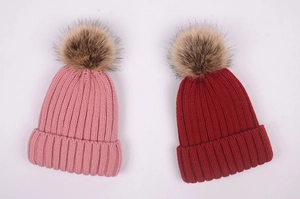 Detailed close-up of pink and red knit beanies with fluffy faux fur pom-poms on top