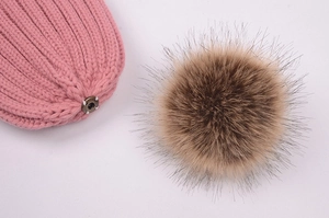 Detail of a pink knit beanie featuring a detachable fluffy brown faux fur pom pom attachment